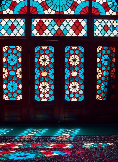 an intricate geometric patterned glass window in an old persian house, colorful light shining through the windows onto Persian carpet on floor below, red and blue hues, beautiful --ar 93:128