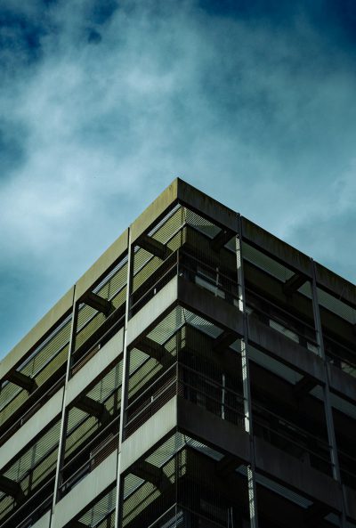 A photograph of an urban building with balconies, taken from the ground looking up at it. The sky is blue and cloudy. In a cinematic style, with soft lighting from a low angle shot, captured in the style of Hasselblad X2D camera using Kodak Vision3 50d film stock. --ar 43:64