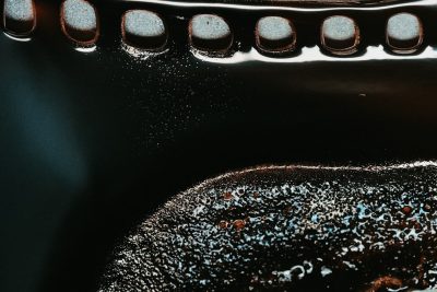 A closeup of the inside bottom edge of an iron cast pan, filled with oil and black coffee powder. The camera angle is from above at eye level, focusing on details like metal textures and small bubbles. It's a dark room with a soft light source highlighting these features. The image is in the style of gas flame. --ar 128:85