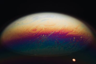 A close up of the surface of Jupiter, shot on film, with atmospheric rainbow colors against a black background, with fluid and organic shapes in the style of dark teal and orange. --ar 128:85