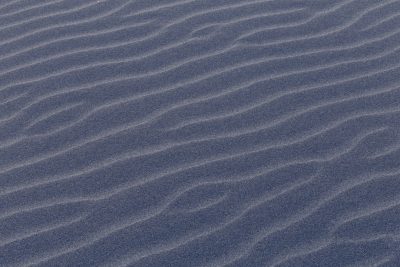 A high-resolution texture of sand ripples, captured from above in the desert at dusk. The textured surface is navy blue with subtle gray patterns and lines that create an abstract pattern reminiscent of ocean waves. It is a tranquil yet mysterious background for design projects. --ar 128:85