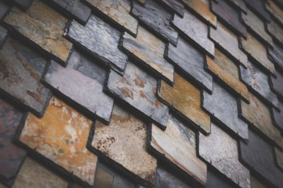 A close-up of the slate shingle wall, showcasing its unique texture and color palette. The pattern is intricate with different shades of gray, brown, and yellow, creating an artistic visual effect in the style of the wall. --ar 128:85