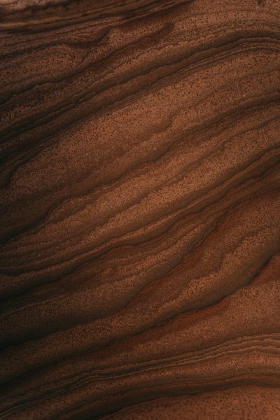 A closeup of the texture of walnut wood, showcasing its rich brown tones and natural grain patterns. The background is a softly focused that enhances the details in the foreground. This design creates an elegant atmosphere with warm hues and intricate textures for use as a backdrop or wallpaper. A softly blurred view of a light red desert landscape in the distance. The composition focuses on capturing the beauty in the style of s750w. --ar 85:128
