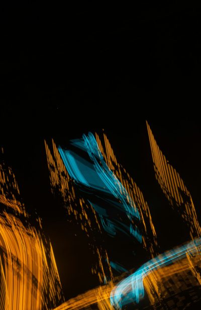 abstract light trails in the shape of buildings on a black background, with orange and blue colors, presented simply and minimally with motion blur in a low angle shot. --ar 83:128