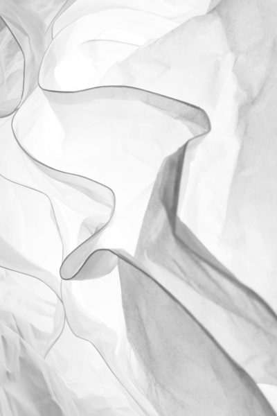 White paper, crumpled and draped in soft waves creating an abstract pattern with delicate folds and subtle texture. The monochromatic color scheme adds depth to the minimalist composition, highlighting intricate details that suggest movement and fluidity within its simplicity. --ar 85:128