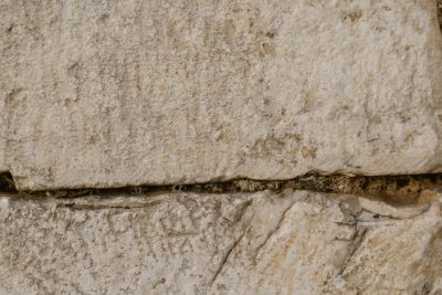 A closeup of the ancient Greek stone wall, showing signs of wear and tear with small cracks in its surface, highlighting textures that add depth to historical buildings. The photo was shot on a Sony Alpha A7R IV in the style of historical documentation. --ar 128:85