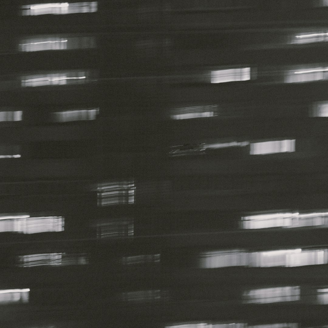 A black and white photo showing motion blur, lights in windows at night time with film grain and an analog photography style. Glitch art and minimalism make the image blurry and hazy.