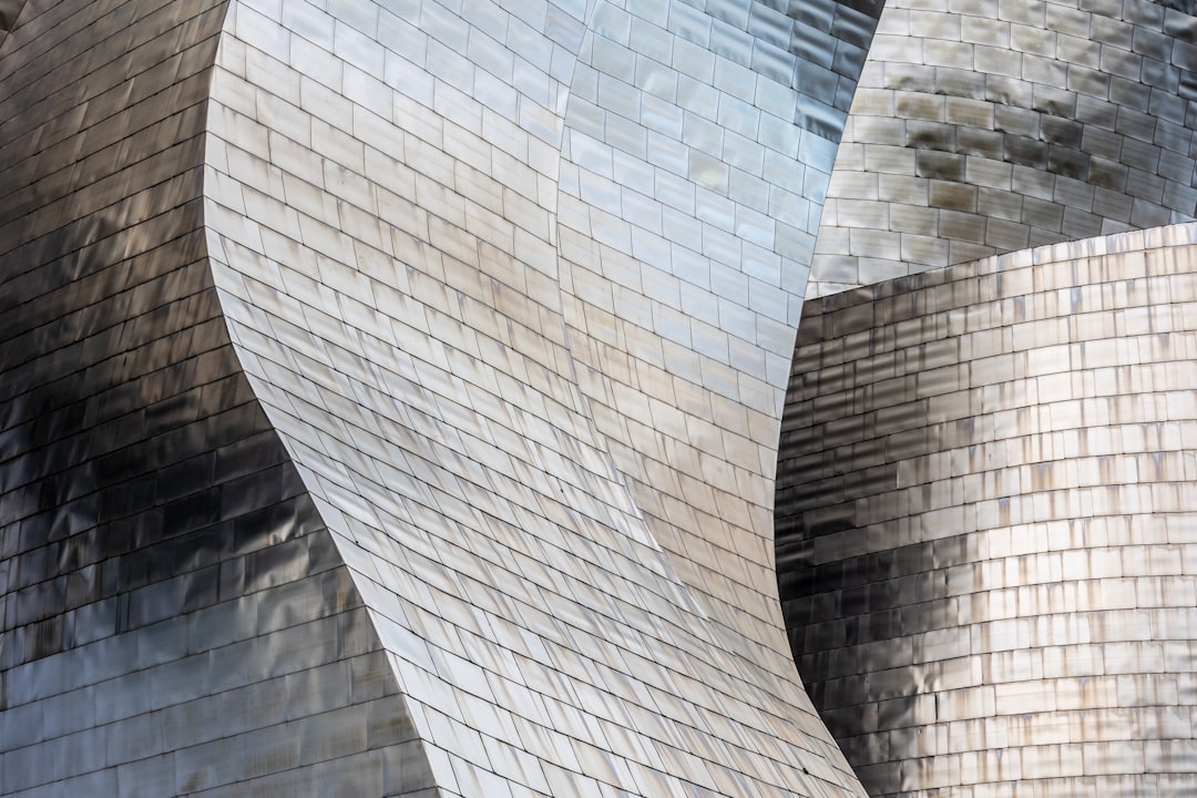 A closeup of the iconic Guggenheim building in the Basque style, made from shiny silver metal tiles, showcasing detailed textures and reflections on its surface. The focus is set at an angle to capture the unique architectural design. Shot with a Canon EOS R5 for sharpness and clarity. –ar 128:85