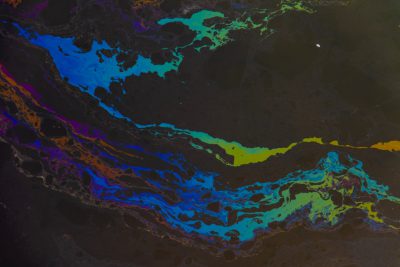 A top-down view of an oil slick on water, with vibrant colors representing different elements and black ink, creating a striking contrast against the dark background. The intricate patterns formed by the flow and fusion of liquid, adding depth to the composition. This visual representation is reminiscent of environmental art, emphasizing color play in a dynamic manner. It symbolizes both beauty and data visualization, showcasing natural elements through digital creation in the style of environmental art. --ar 128:85