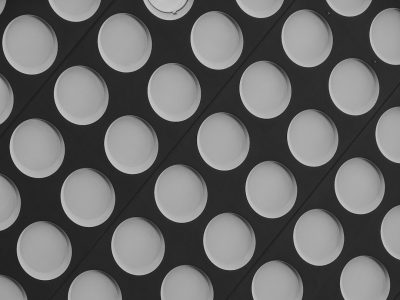 A black and white pattern of large, circular holes on the surface of an industrial building, creating a modern abstract background with geometric shapes. The composition is symmetrical, with each hole arranged in rows at precise angles to create visual depth. Soft lighting casts gentle shadows through these dots, adding contrast between light gray areas and dark surfaces. This minimalist design adds texture and detail while evoking contemporary architectural elements in the style of modern abstract art. --ar 4:3