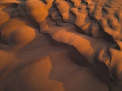 Aerial view of the dunes at sunset, with warm hues and intricate patterns in shades of orange and brown. The sand is textured like fine fabric under soft light, creating an otherworldly atmosphere. --ar 4:3