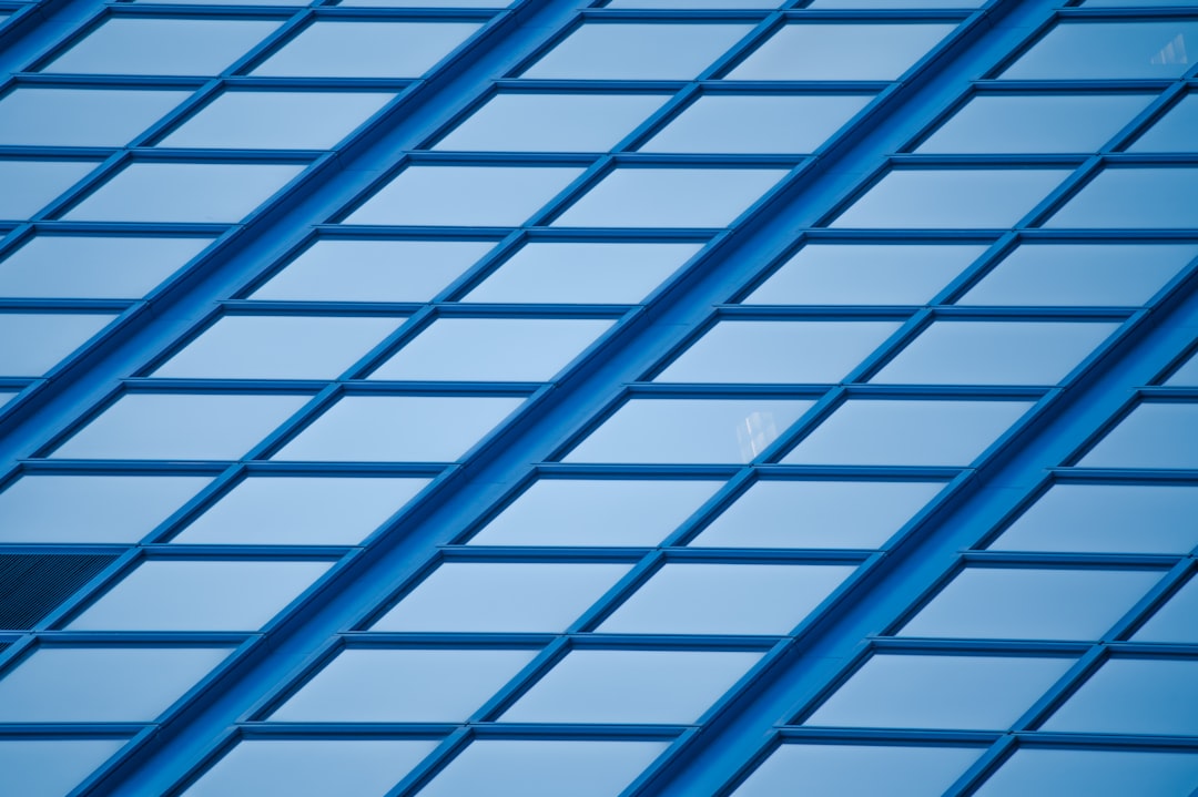 A blue glass building with diagonal grid lines in a minimalist style, closeup shot, high resolution photography, symmetrical composition, daylight, cool tone, focused on the geometric patterns of windows and steel frames. –ar 128:85