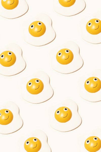 little smiley face fried eggs pattern, white background, yellow and orange colors, simple illustration, high resolution photography, minimalist style, graphic design poster art, pop-inspired shapes, textured surface details, crisp clean lines, in the style of graphic design --ar 85:128