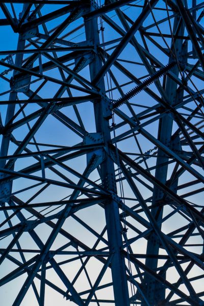 A close up of the steel structure underneath an electric pole. The photo has a darker blue color sky background and was taken with Provia film. It is hyperdetailed in the style of Willie Nath. --ar 85:128