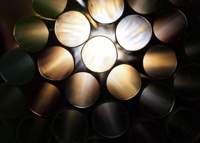 A close up of an array of round metal pipes, lit from above by the sun in a dark room. The light is coming through the holes and illuminating them with a warm glow. In front there is one pipe that has been painted white. It reflects some of the other colors in the style of the artist. --ar 128:91