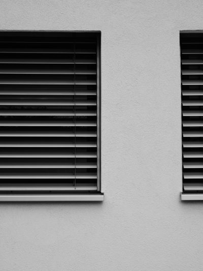 A minimalist black and white photo of two windows with blinds on the side of an empty grey wall. The photo is in the style of a minimalist artist. --ar 3:4