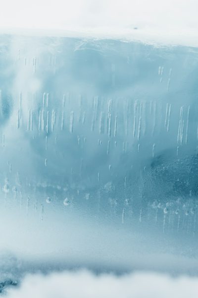 A photo of a close-up shot of an ice wall, covered in raindrops, with soft blue and white tones, a foggy background, taken with a Canon EOS R5 at F2, ISO30, and 89MM. Soft lighting creates a misty, atmospheric, and ethereal dreamlike style. --ar 85:128