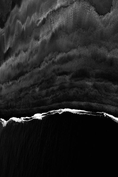 Black sand beach, drone shot, stormy clouds overhead, black and white, high contrast, stark, minimalist, sleek, textured, abstract, atmospheric, dark, mysterious, ethereal, surreal, powerful, moody. --ar 85:128