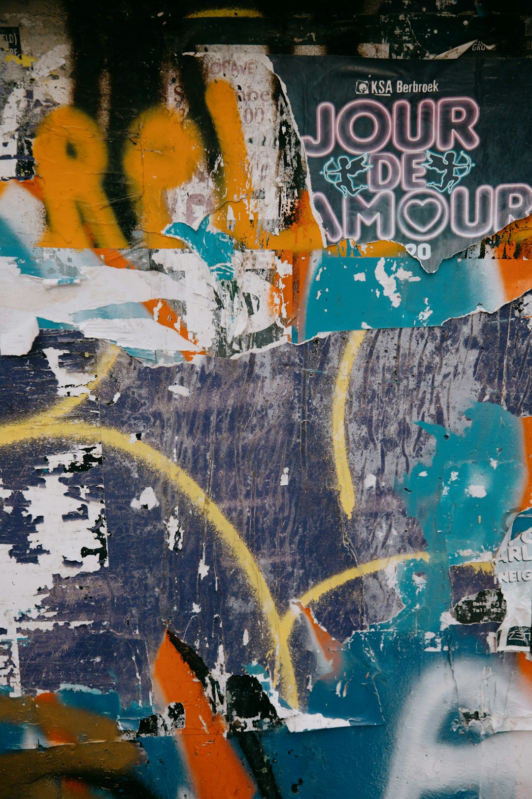 colorful graffiti wall with the text “J故意 OUr de Amour” written in blue, orange and yellow on it, the background is dark, the colors of graffitti can be seen through an old ripped poster –ar 85:128