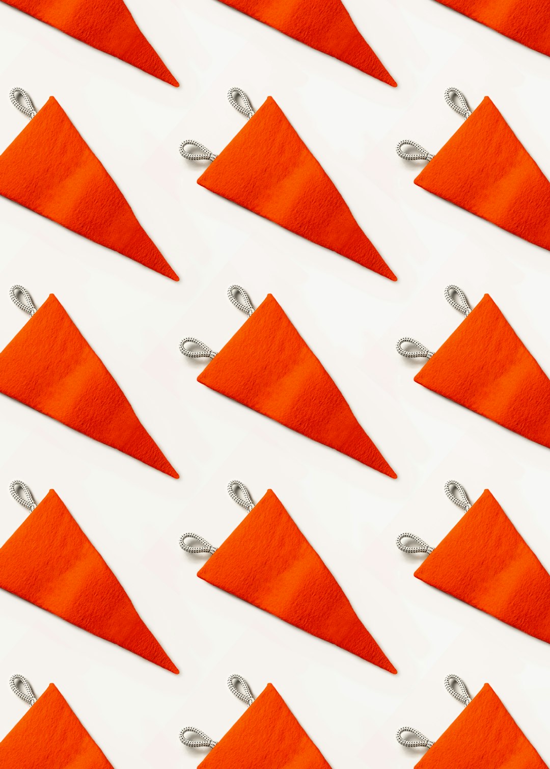 A pattern of small orange triangular fabric flags, with silver edging on the corners and sides, white background, flat lay photography, minimal concept, photographed in the style of art director. –ar 91:128