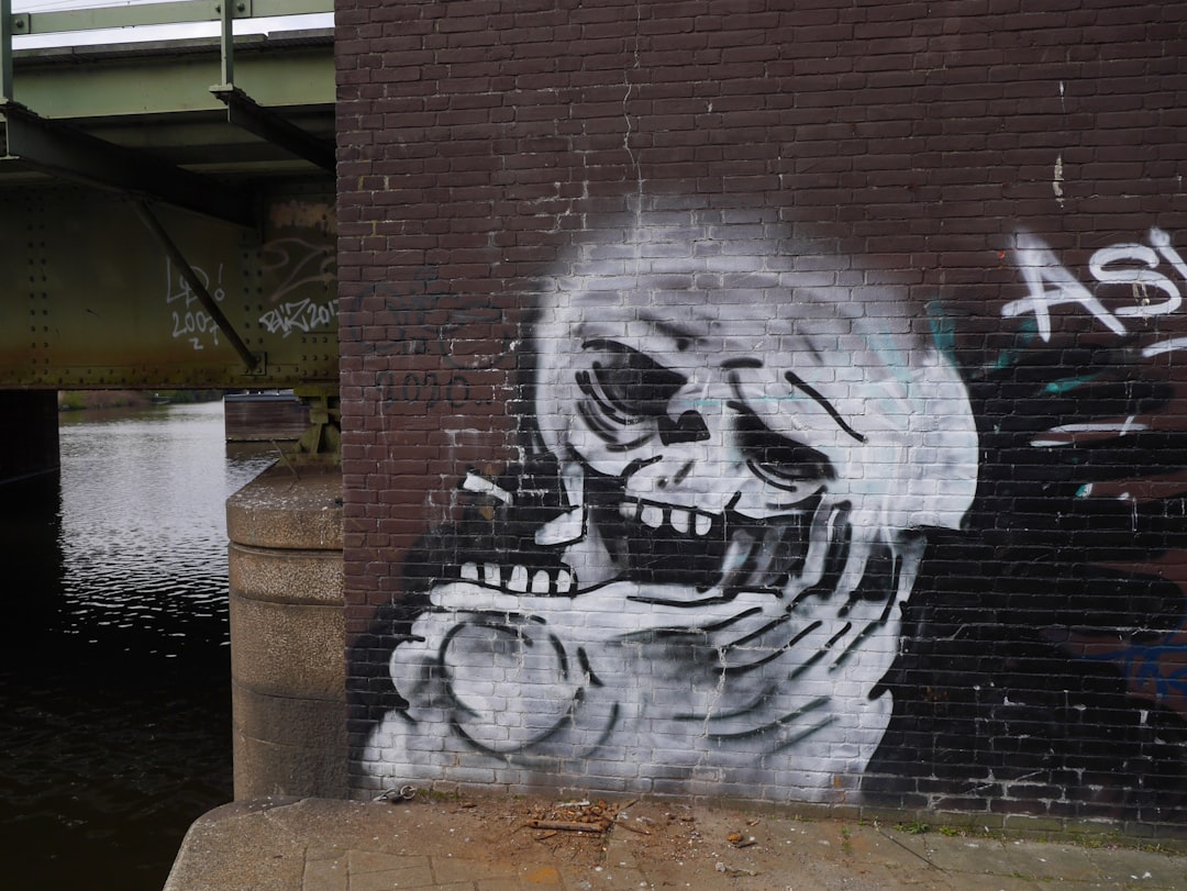 Graffiti of a laughing skull smoking on the wall next to a river, under a bridge in Amsterdam in the style of [Banksy](https://goo.gl/search?artist%20Banksy). –ar 4:3