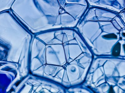 A close up photo of blue soap bubbles with a hexagonal structure against an abstract background, done in the macro photography style showing intricate texture and glassy surface details, with light refraction and reflections and a shallow depth of field captured at high resolution and high definition. --ar 64:47