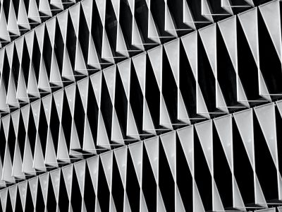 A closeup of the pattern on an exterior building, capturing its geometric shapes and angles in monochrome tones. The focus is on intricate details like triangular patterns or fluted textures that create visual interest. This shot emphasizes architectural design with a modern aesthetic. Shot in the style of Nikon D850 camera using Nikkor 2470mm f/6.3E ED VR lens. --ar 4:3