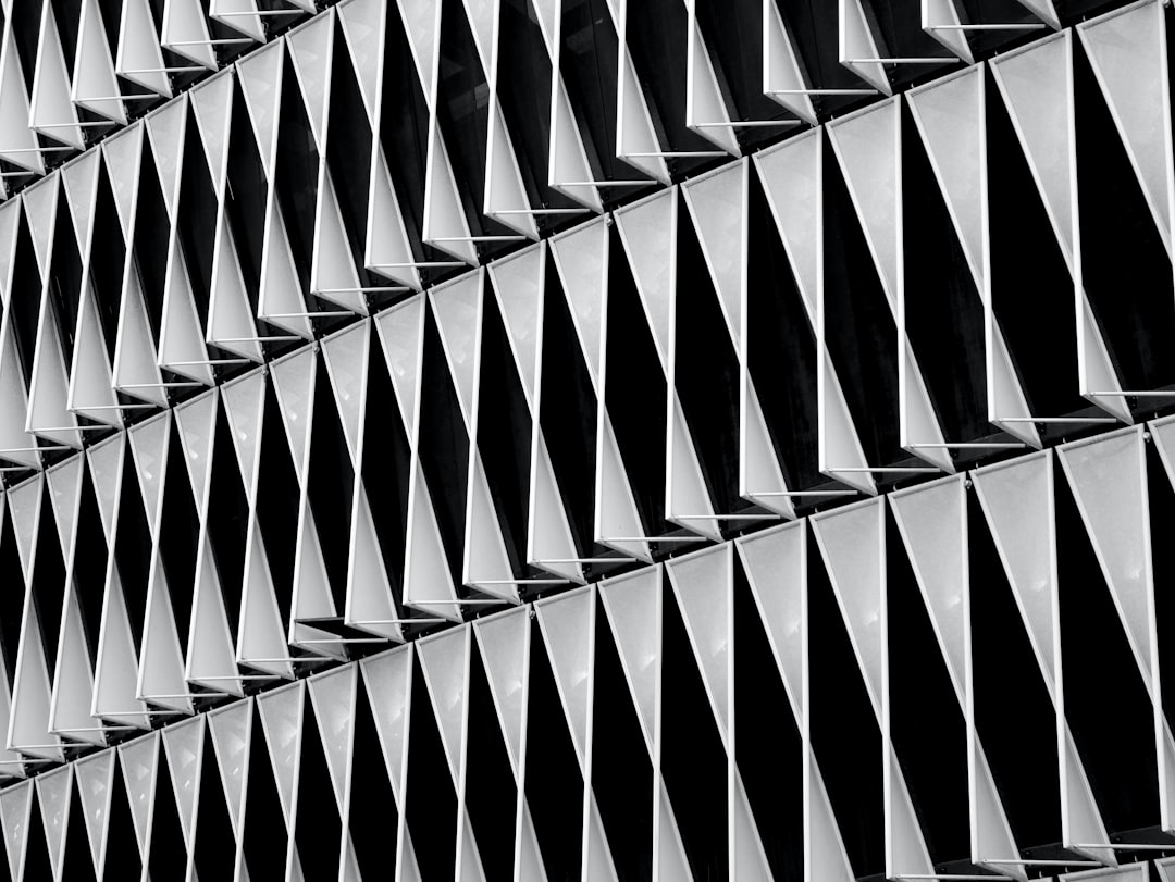 A closeup of the pattern on an exterior building, capturing its geometric shapes and angles in monochrome tones. The focus is on intricate details like triangular patterns or fluted textures that create visual interest. This shot emphasizes architectural design with a modern aesthetic. Shot in the style of Nikon D850 camera using Nikkor 2470mm f/6.3E ED VR lens. –ar 4:3