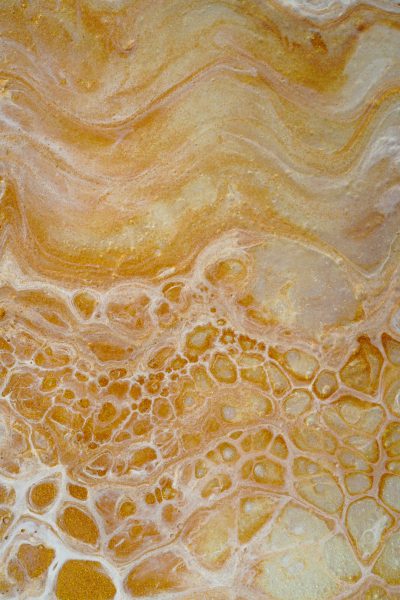 A closeup of the surface texture of marble, showcasing its intricate patterns and warm tones in shades of orange and yellow. The pattern is made up of delicate swirls that give it an elegant appearance. Inhale, intricate lines of swirling colors on top. Top view, light background, natural lighting, hyperrealistic photography. --ar 85:128