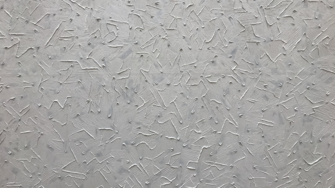 A closeup of the texture on an smooth, gray wall with small and large crisscross lines that resemble splashes or strokes in various sizes. The background is uniform and bright white to highlight details. –ar 16:9