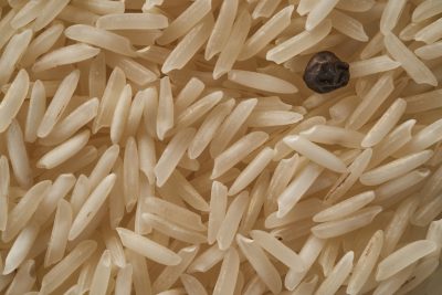 Closeup of long grain rice, with one single black pepper seed visible in the middle. The texture is detailed and realistic, showcasing each tiny grain of brownish white color. This shot captures an overhead view of the grains from above, emphasizing their natural shape and size against a neutral background. The focus on individual rice pieces adds depth to the composition, creating visual interest and highlighting its pure form as they stand out amidst other white or yellow rice. This image is in the style of realistic texture photography, showcasing each tiny grain. --ar 128:85