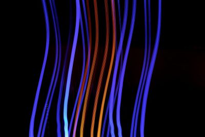 A dark background with colorful blue and orange lines of light that form the shape of an electric cable, long exposure photography techniques, vanishing point composition style, digital artwork, black background, bokeh lighting effect, high resolution image, wide angle lens perspective, motion blur effects, vibrant colors, dynamic lighting. --ar 128:85