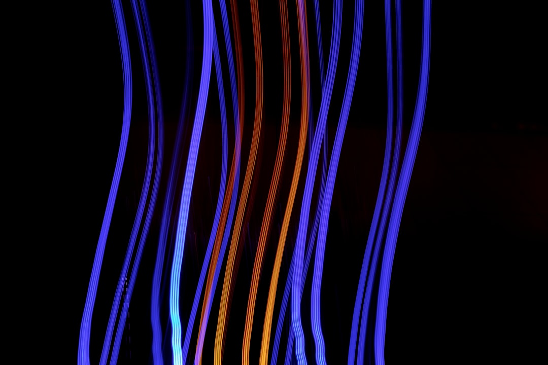 A dark background with colorful blue and orange lines of light that form the shape of an electric cable, long exposure photography techniques, vanishing point composition style, digital artwork, black background, bokeh lighting effect, high resolution image, wide angle lens perspective, motion blur effects, vibrant colors, dynamic lighting. –ar 128:85