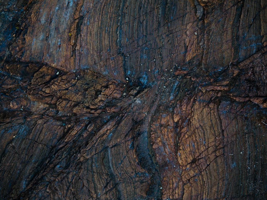 top down drone photo of the texture and patterns on an old weathered rock surface, dark blue, black and brown colors, organic lines, sharp focus, high resolution photography in the style of nature. –ar 128:95