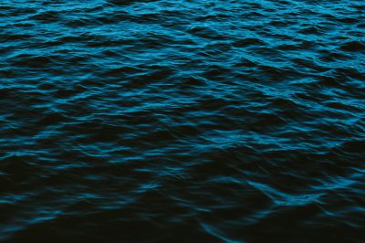 A dark blue sea, with ripples on the surface, top view, in the style of photography, minimalist background, no people or objects in sight, low light environment, soft lighting, focus on the water texture and color, high resolution. --ar 128:85