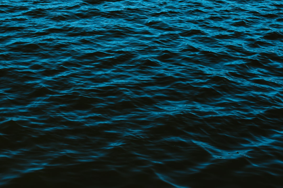 A dark blue sea, with ripples on the surface, top view, in the style of photography, minimalist background, no people or objects in sight, low light environment, soft lighting, focus on the water texture and color, high resolution. –ar 128:85