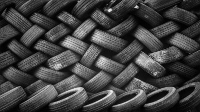 A black and white photograph of an array of used tires arranged in a pattern, creating the illusion that they form a large wicker basket full of flats. The background is a simple monochrome color to highlight the texture and patterns on each tire. --ar 16:9