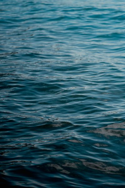 The water surface is calm, with gentle ripples on the deep blue sea background. The details of light waves were captured using a Nikon D850 camera with a Nikon AFS vieux lens at an f/22 aperture setting, with an ISO speed of 400, in high resolution. This photo was taken in the style of photographer Canon EOS7D Mark II, presenting the water texture with a shallow depth of field. It creates a serene atmosphere with a cinematic feel. --ar 85:128