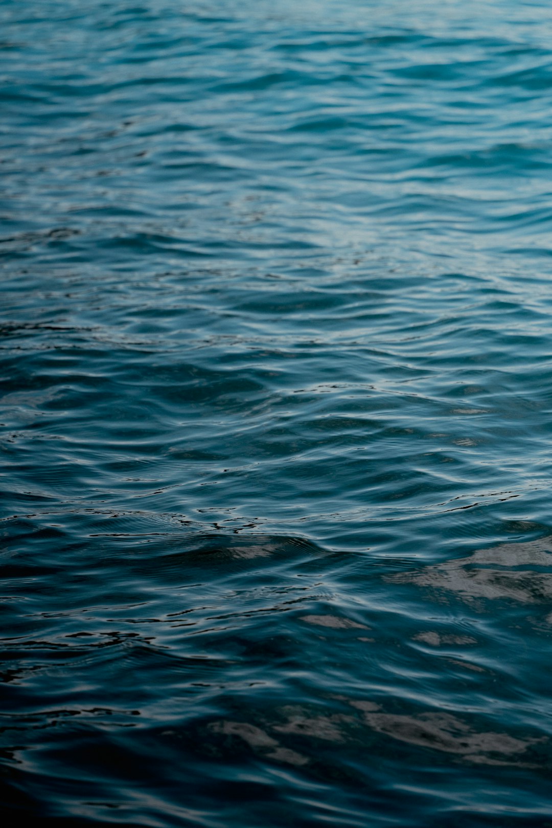 The water surface is calm, with gentle ripples on the deep blue sea background. The details of light waves were captured using a Nikon D850 camera with a Nikon AFS vieux lens at an f/22 aperture setting, with an ISO speed of 400, in high resolution. This photo was taken in the style of photographer Canon EOS7D Mark II, presenting the water texture with a shallow depth of field. It creates a serene atmosphere with a cinematic feel. –ar 85:128