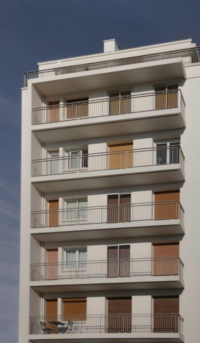 A clean white modern building with balconies, with wooden shutters on the balcony doors, with one floor slightly higher than other floors, in shades of brown and beige colors, against a dark blue sky, photo realistic, taken in the style of Canon EOS. --ar 37:64