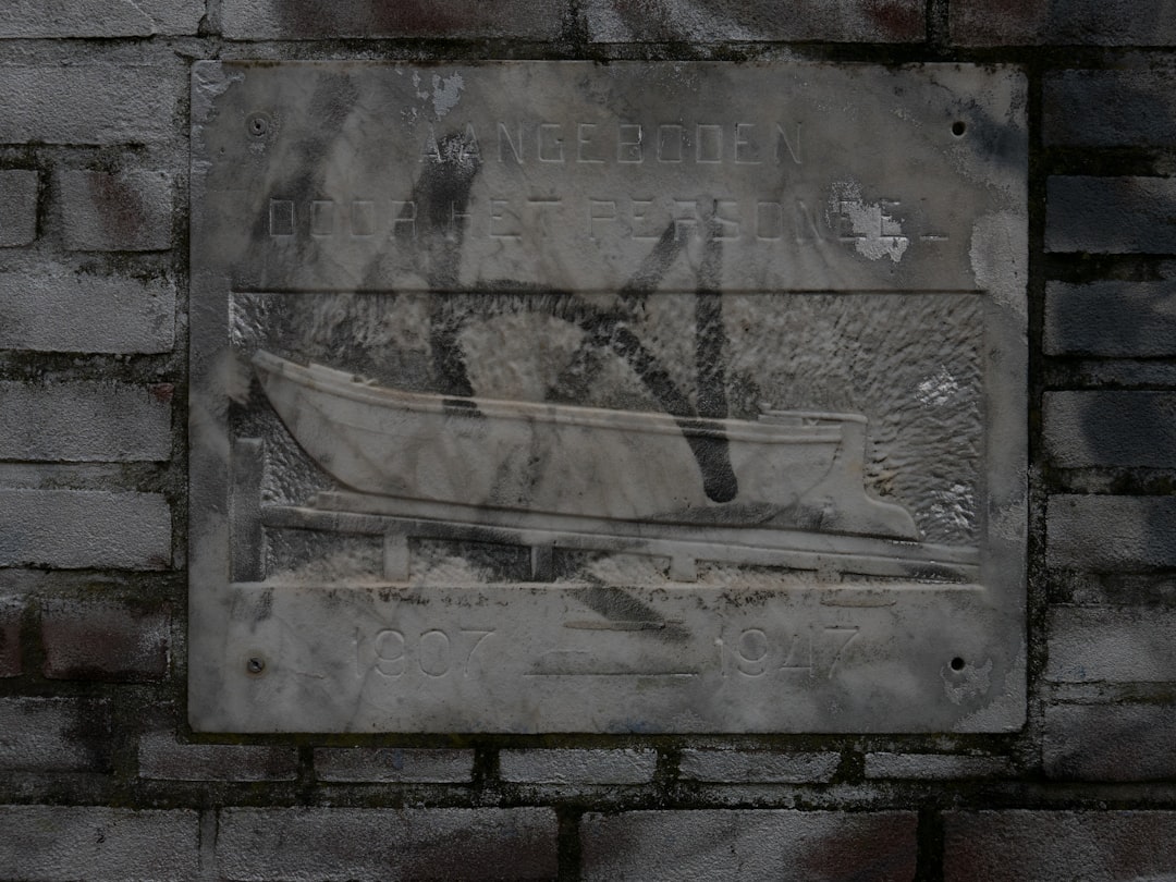 A stone slab with the inscription “Kangonden” and an engraving of small boat on it, is mounted against a gray brick wall. The text reads in Dutch ‘ik kijkt op de watermerk van brood macrophotography –ar 4:3