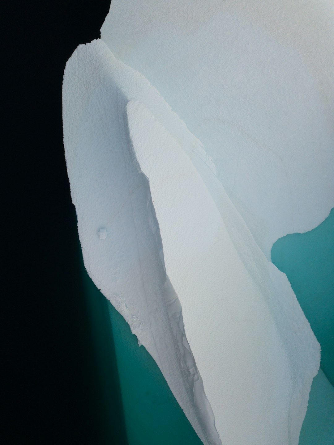 A close-up photograph of an iceberg in the style of James Arrondel, with a minimalist and aerial view style, featuring green and blue tones and white snow, composed of simple shapes with high contrast and high resolution. –ar 95:128