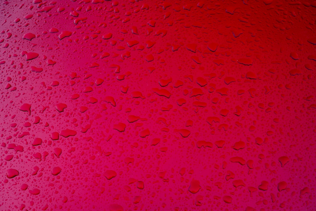 Red background with water droplets, top view, pink red gradient background, closeup of the surface of car body parts, textured and patterned, bright colors, delicate texture, water drops on glass windows, highdefinition photography, wideangle lens, natural light, static composition. –ar 128:85