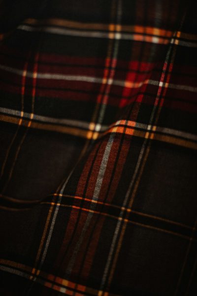 A close-up shot of the dark red, black and yellow tartan pattern on fabric with visible threads and textures, highlighting its intricate design and texture. The atmosphere evokes nostalgia for retro fashion, with warm lighting accentuating each thread and line, creating a nostalgic mood for product photography. --ar 85:128