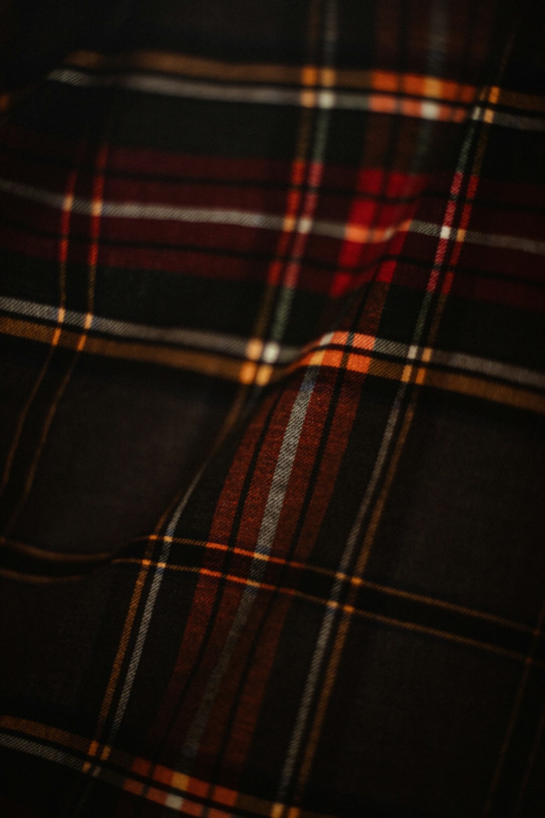 A close-up shot of the dark red, black and yellow tartan pattern on fabric with visible threads and textures, highlighting its intricate design and texture. The atmosphere evokes nostalgia for retro fashion, with warm lighting accentuating each thread and line, creating a nostalgic mood for product photography. –ar 85:128