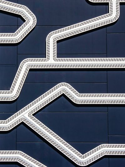 A closeup of the architectural details on an industrial building, featuring white lines and curves on dark blue metal panels. The design includes geometric shapes inspired by train tracks or paths, adding depth to its appearance. This is captured in high resolution with a macro lens, showcasing intricate patterns that add visual interest to the structure's exterior. The composition emphasizes the unique textures and forms, creating a visually appealing urban landscape in the style of train tracks or paths. --ar 3:4