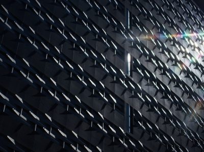 A building facade with triangular patterns and a geometric design. Sun rays reflecting off the surface in a closeup shot of urban architecture. The photography focuses on architectural details highlighted by sunlight in the style of professional photographs with dark tones and high resolution. --ar 128:95