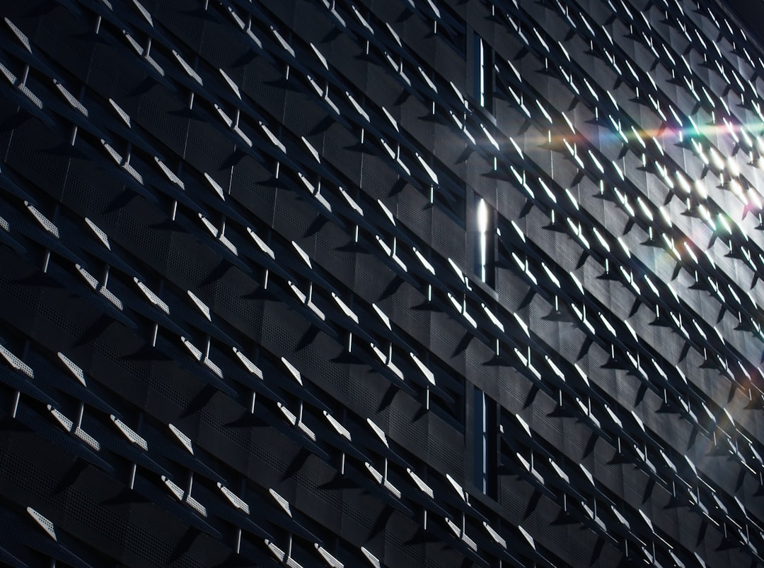 A building facade with triangular patterns and a geometric design. Sun rays reflecting off the surface in a closeup shot of urban architecture. The photography focuses on architectural details highlighted by sunlight in the style of professional photographs with dark tones and high resolution. –ar 128:95