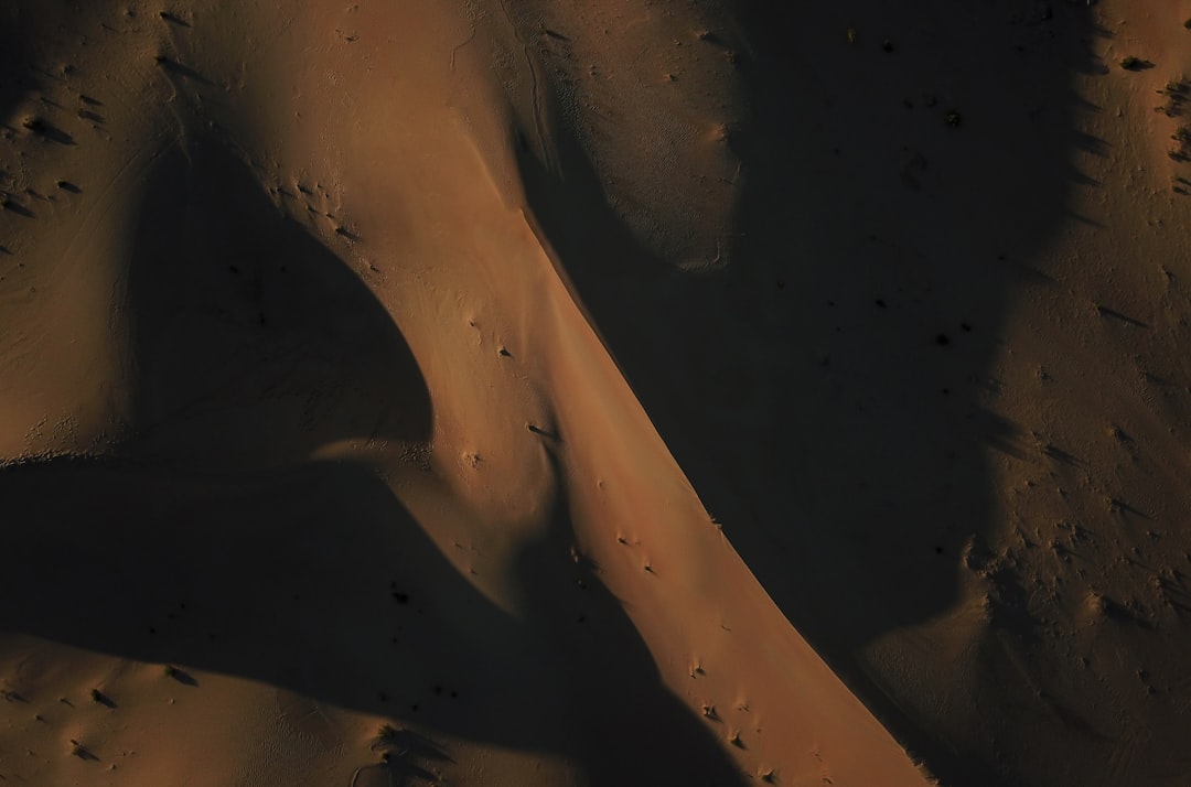 Aerial view of shadows cast on the sand dunes in an empty desert, dramatic shadows, cinematic, shot in the style of ARRIFLEX35 BL camera, stock photo contest winner, professional photography, sharp focus, high resolution. –ar 32:21