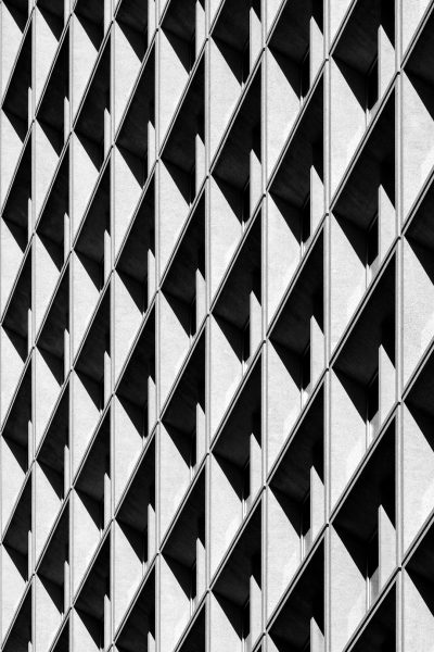 A black and white photograph of the exterior wall texture of an office building, showcasing symmetrical grid patterns with triangular shapes, creating geometric harmony. The composition is balanced, highlighting architectural details in high contrast in the style of the artist. --ar 85:128